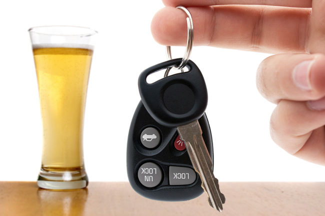 car keys are held in front of a tall glass of beer