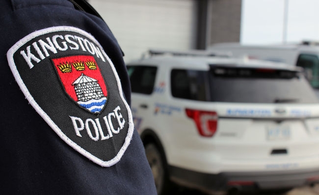 Kingston police badge in the foreground, with a police vehicle in the blurred background.