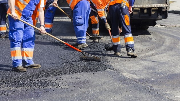 Construction workers spread asphalt over a cracked roadway in this file photo.