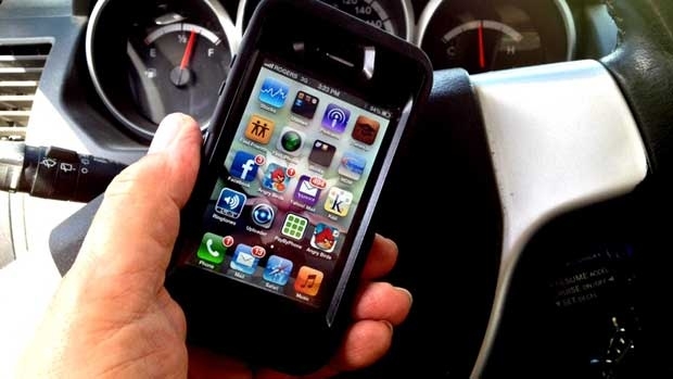 A person holds an iPhone behind the wheel of a vehicle.